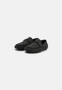 Sorte slip-on sko lavet af et blødt tekstureret materiale, med en forlænget tåform, dekorative flettede detaljer og en fleksibel gummisål.
