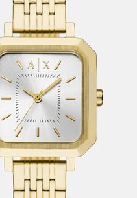 Reloj de pulsera cuadrado dorado con esfera plateada, marcadores de hora dorados y manecillas que marcan las 10:10:35, con el logo "A|X" a las 12 en punto.