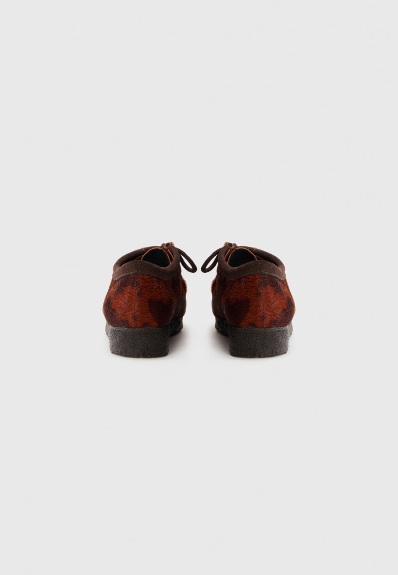 Braune Wildlederschuhe mit einem strukturierten Muster, dunkelgrauen Sohlen und Schnürdetails hinten. Rundspitze und niedriges Absatzdesign.
