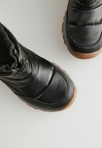 Bottes noires imperméables avec une tige en cuir lisse, conçues avec une isolation, un bout rond et une semelle en caoutchouc texturé pour une meilleure adhérence.