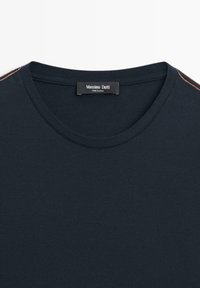 T-shirt blu scuro con tessuto strutturato, caratterizzato da una scollatura rotonda e cuciture arancioni a contrasto sulle spalle. Etichetta Massimo Dutti visibile.