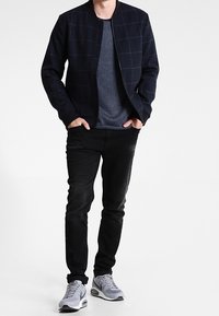 Marininspirerad bomberjacka med rutmönster, grå t-shirt med rund hals, svarta slim-fit jeans och grå sportskor.