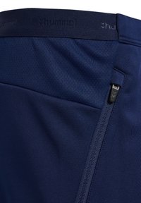Pantalones cortos deportivos de color azul marino, fabricados en tejido suave, con una cinturilla texturizada y un bolsillo con cremallera en el lateral. Logo de Hummel visible.