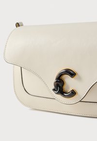 Borsa in pelle beige chiaro con patta curva, caratterizzata da una fibbia con logo nero e oro e cuciture a contrasto lungo i bordi.