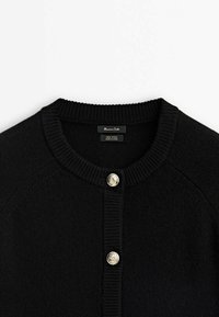 Cardigan en laine noire avec encolure ronde côtelée et deux boutons dorés décoratifs sur la patte de boutonnage avant, étiquette visible à l'intérieur du col.
