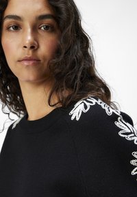 Suéter negro con diseños florales bordados en blanco en los hombros, cuello redondo y tejido texturizado. Enfoque en primer plano en el cuello.
