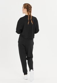 Svart kortad sweatshirt och matchande byxor i mjukt tyg, med långa ärmar, sidofickor och ribbade muddar. Vita sneakers fulländar outfiten.