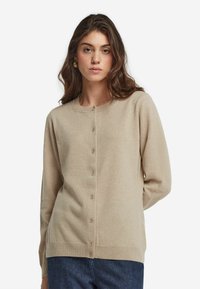 Beige cardigan i mjukt tyg, med rund halsringning och knappslå framtill, långa ärmar och en avslappnad passform.