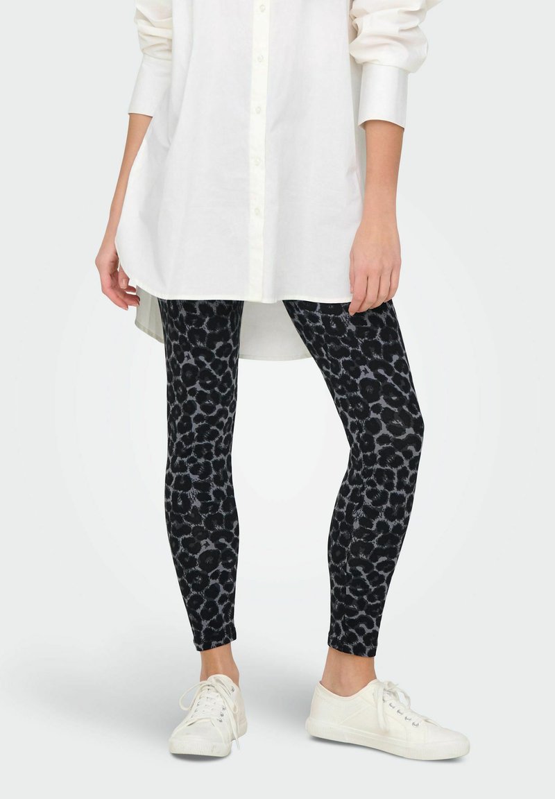 Svarta leggings med ett mönster i leopardtryck, tillverkade av stretchigt material. Bärs med en oversize vit skjorta och vita sneakers.