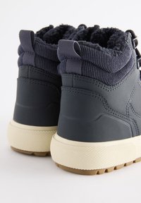 Stivaletti alla caviglia blu scuro con tomaia strutturata, dotati di una fodera pelosa, tirante posteriore e suola in gomma color crema con battistrada decorato.