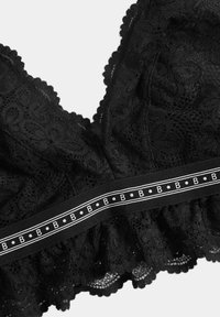 Soutien-gorge en dentelle noire avec des motifs floraux, des bords en scallop et une bande élastique décorative avec des accents blancs.
