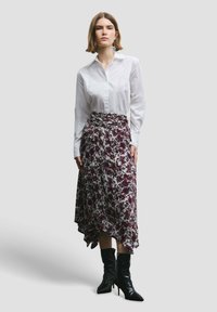 Witte button-up shirt gecombineerd met een asymmetrische rok tot de knie met een bloemenpatroon in tinten bordeauxrood en wit, gedragen met zwarte hoge hakken.