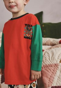 Langärmliges Shirt in Rot und Grün mit einem Rentier-Graphic und dem Aufdruck "Team Rudolf". Aus Baumwolle, mit gerippten Bündchen und entspanntem Schnitt.