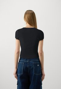 Črni rebrasti kratkosleeveni top z okroglo ovratnikom, kombiniran s temno modrimi jeans hlačami, ki imajo žepe s krpicami in oznako na hrbtni strani.