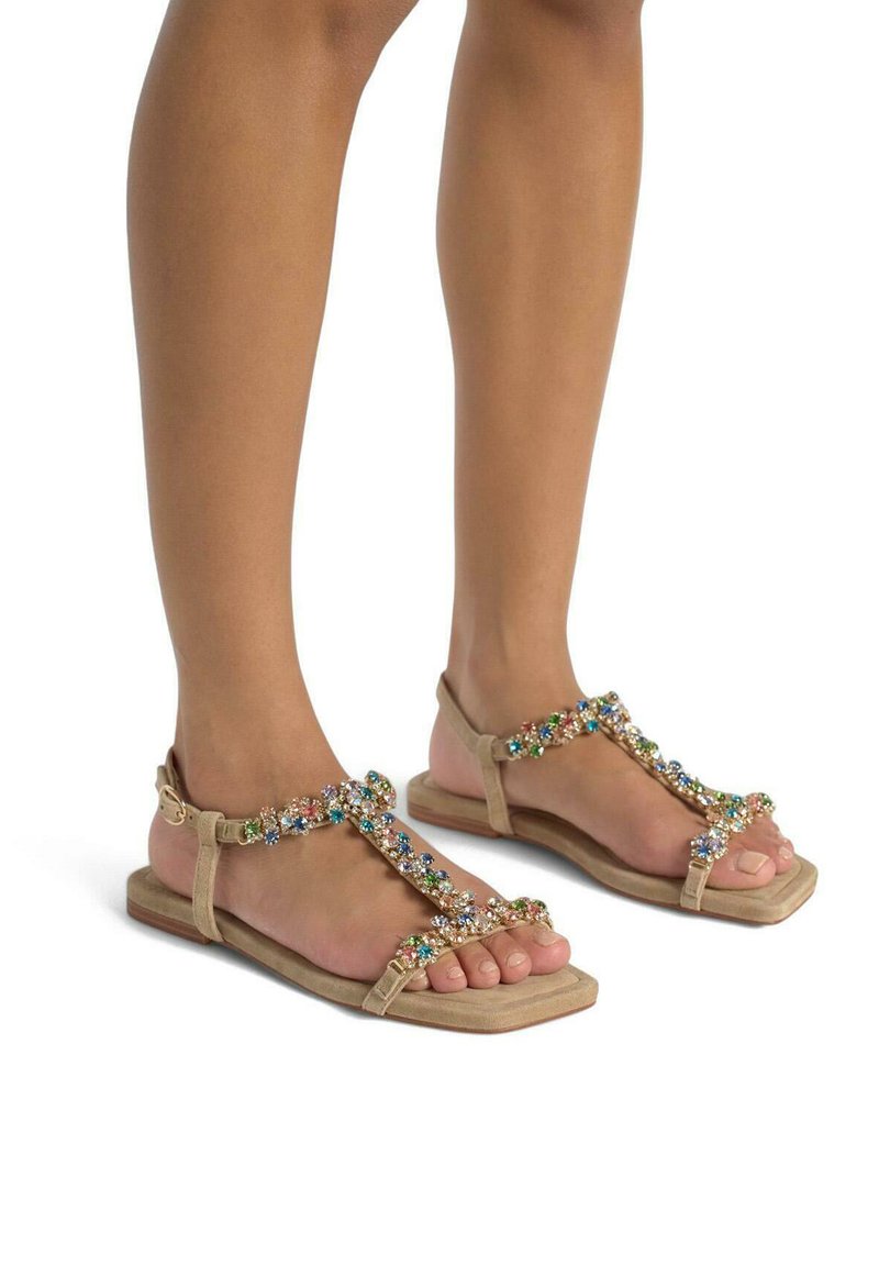 Sandali beige con suola piatta, caratterizzati da un design a T decorato con strass colorati e una fibbia per la regolazione.