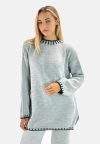 Suéter de punto gris claro con cuello y puños negros acanalados, aberturas laterales y un acabado texturizado. Corte casual y oversized con mangas largas.