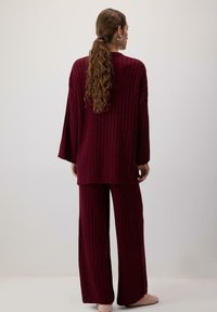 Burgundské žebrové pletené lounge set se skládá z dlouhého rukávu a kalhot širokého střihu. Měkká textura s volným střihem. Nosit s pantofli svých světlých barev.