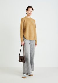 Beige knit sweater, gray wide-leg jeans, silver sneakers, and a small brown crossbody bag with gold hardware. Smooth texture throughout.