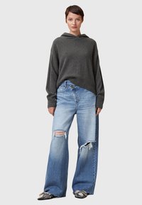 Grå huvtröja med avslappnad passform, matchad med ljusblå vida jeans med slitna detaljer och fransade nederkanter. Svarta mönstrade skor.