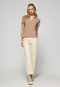 Beżowa koszulka polo, krótki rękaw, kołnierzyk, delikatny detal z logo. Połączona z kremowymi spodniami w szerokim kroju i beżowymi trampkami. Gładka tekstura materiału.