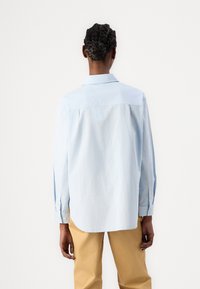 Camicia azzurro chiaro a maniche lunghe con colletto button-down, vestibilità rilassata e orlo arrotondato. Indossata con pantaloni color khaki.