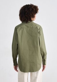 Olivenfarget langermet skjorte med knappede krage, lett buet hem og mansjetter med knapper. Laget av et glatt, lett materiale.