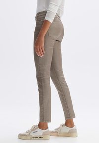 Khaki Skinny Jeans mit glatter Textur, Fünf-Taschen-Design und subtilen Verblassungen. Kombiniert mit weißen und beigen Sneakers.