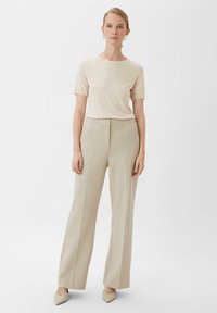Beżowa bluzka z krótkim rękawem połączona z jasnobeżowymi, wysokimi, szerokimi spodniami. Buty to blade, szpiczaste szpilki. Prosty design i faktury.