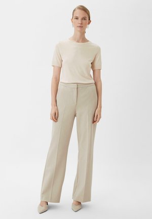 Beige Kurzarmoberteil kombiniert mit hellbeigen, hoch taillierten, weiten Hosen. Die Schuhe sind blass, mit spitzem Zehenbereich. Einfaches Design und Texturen.