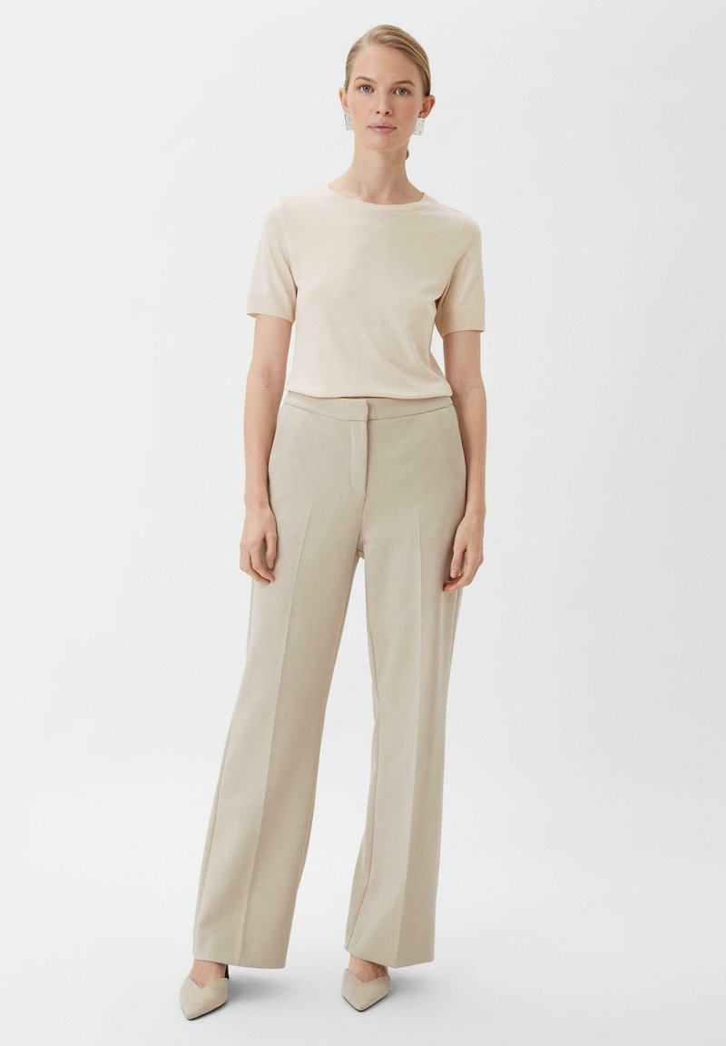 Beżowa bluzka z krótkim rękawem połączona z jasnobeżowymi, wysokimi, szerokimi spodniami. Buty to blade, szpiczaste szpilki. Prosty design i faktury.