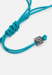 Bracelet en corde tressée turquoise avec une fermeture métallique présentant un design géométrique. La texture de la corde est lisse, et la fermeture a une finition polie.