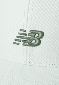 Casquette vert clair en tissu texturé, avec un logo New Balance brodé en vert foncé sur le devant. Détails de couture visibles.