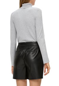 Grauer Rollkragenpullover mit langen Ärmeln, kombiniert mit hochgeschnittenen schwarzen Leder-Shorts mit glatter Textur und zwei Gesäßtaschen.