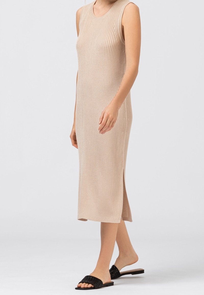 Abito midi in maglia a coste beige con scollo rotondo, design senza maniche e spacco laterale; indossato con sandali neri intrecciati.
