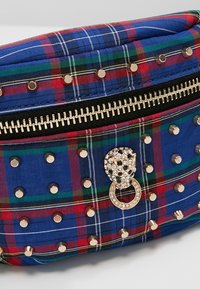 Tartan-mönstrad väska i blått, rött och grönt, med gyllene nitar och en distinkt juvelprydd hårdvaruaccent samt dragkedjestängning.