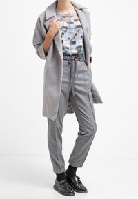 Cappotto grigio oversize, top leggero blu a fantasia, pantaloni grigi a gamba affusolata e scarpe in pelle nera con cinturino. Texture morbide e design casual.