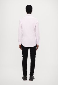 Camisa de manga larga de color rosa claro con un sutil patrón de rayas, combinada con pantalones negros de corte ajustado y calzado negro. Vista posterior que muestra los puños abotonados.