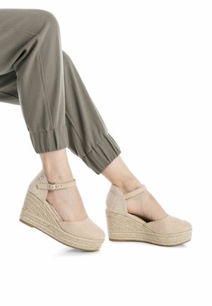 Zapatos de cuña beige con suelas de yute estilo espadrille, paneles laterales texturizados y una correa con hebilla alrededor del tobillo.