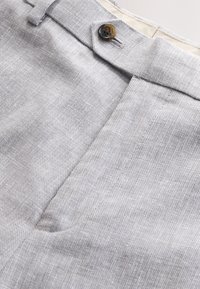Pantalon en tissu texturé gris clair avec une ceinture boutonnée et une fermeture éclair à l'avant.
