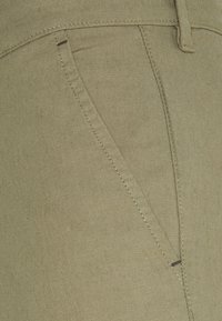 Olivově zelené kalhoty s hladkou strukturou, podrobným šitím a šikmou přední kapsou s jemnými černými akcenty.