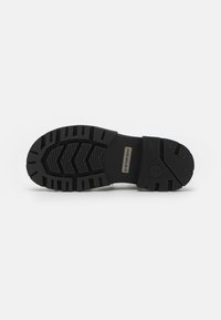 Zwarte rubberen zool met een loopvlakpatroon, voorzien van een gestructureerde afwerking en een metalen logoaccent. Ontworpen voor grip en duurzaamheid.