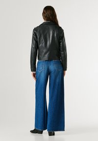 Μαύρο δερμάτινο κοντό μπουφάν με λεία υφή, σε συνδυασμό με φαρδιά μπλε τζιν παντελόνια. Το μπουφάν διαθέτει δομημένους ώμους και κλασικό σχέδιο.