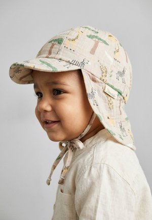 Toddler wearing a beige sun hat with animal prints and a tied chin strap, smiling and dressed in a light-colored shirt.