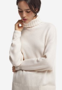 Hellbeiger Rollkragenpullover mit geripptem Kragen und Bündchen. Weiche Textur, überschnittene Schultern und lockere Passform. Vertikale Rippung am Saum.