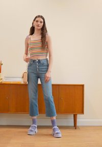 Top cropped às riscas, jeans de cintura alta azul claro, sapatos de plataforma lilás e meias roxas. Armário de madeira natural ao fundo.