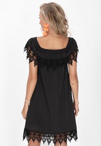 Rochie neagră cu o textură punctată, decolteu off-the-shoulder și detalii din dantelă neagră la mâneci și la tiv. Design simplu, fluid.