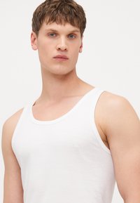 Bjela pamučna majica bez rukava s širokim izrezom i uskim trakama. Glatka tekstura s prilagođenim dizajnom, ističe prsa i ramena.