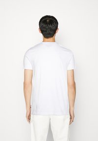Camiseta de algodón blanca con mangas cortas y cuello redondo, que presenta un pequeño logotipo en el lado izquierdo cerca del dobladillo.