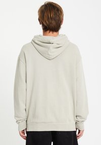 Lys grå hættebluse med en afslappet pasform, snoretræk i hætten og ribbede manchetter. Stoffet ser blødt ud med en glat tekstur.