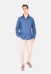 Camicia di jeans blu scuro, con bottoni e maniche lunghe. Combinata con pantaloni beige a pieghe e mocassini beige con nappine. Design semplice e casual.